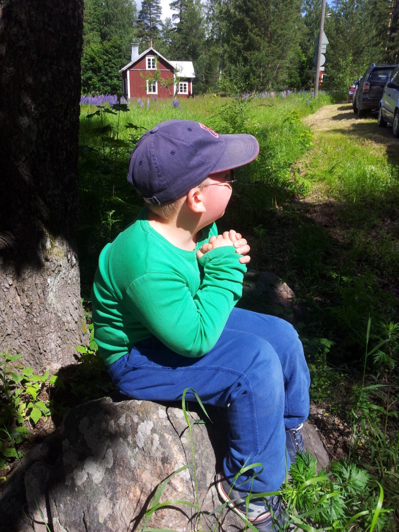 Lippalakkipäinen poika istuu kivellä.