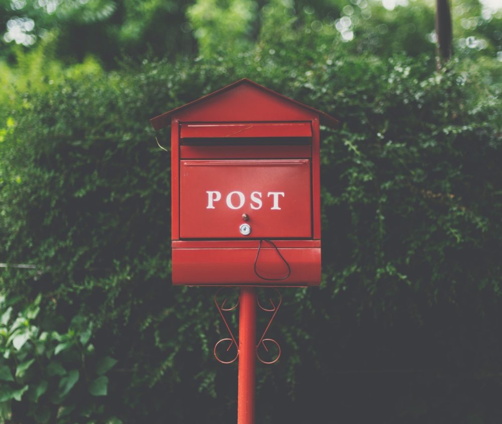 Punainen postilaatikko pensasaidan edessä.